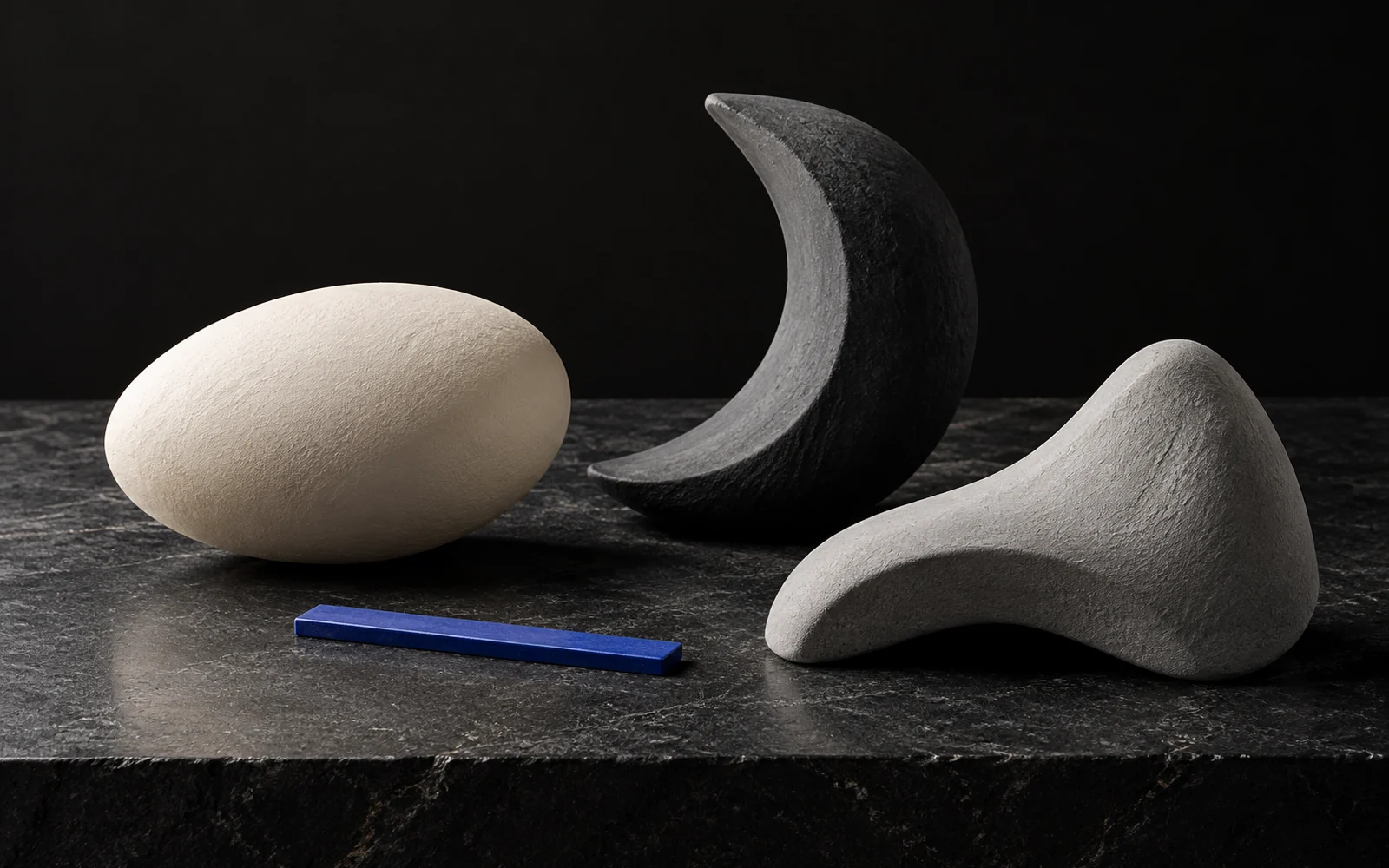 Abstract ivory, charcoal and gray clay forms arranged with a cobalt measuring line to represent shape and facial balance